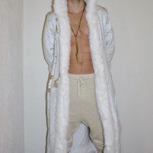 May include: A white hooded robe with faux fur trim and gold sequin accents. The robe is paired with light beige sweatpants. A gold-colored necklace is visible.