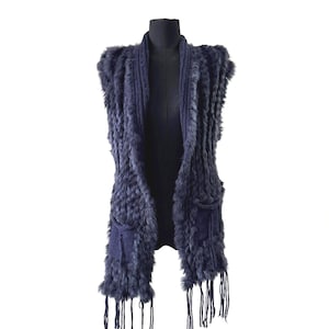 Peut inclure: Un gilet sans manches bleu marine en fourrure texturée. Il comporte deux poches avant et des franges en bas. Le vêtement est présenté sur un mannequin noir sur fond blanc.