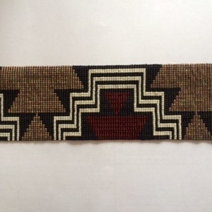 May include: A beaded bracelet with a geometric pattern in black, white, brown, and red. The bracelet has gold metal clasps on either end.