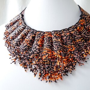 May include: A beaded choker necklace with a geometric pattern in black, orange, and pink. The necklace has a fringe of beads that hangs down from the bottom.