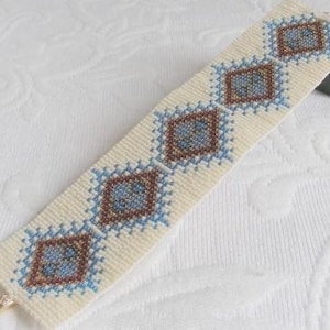 May include: A beaded bracelet with a geometric pattern in shades of blue, brown, and white. The bracelet is made with small seed beads and is woven in a tight, intricate pattern.
