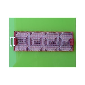 Könnte beinhalten: Ein rotes und weißes Perlenarmband mit einem silbernen Verschluss. Das Armband hat ein geometrisches Muster aus ineinandergreifenden Spiralen.