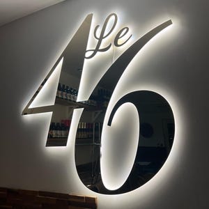 May include: A black and silver illuminated sign with the text "Le 46" in a cursive font.