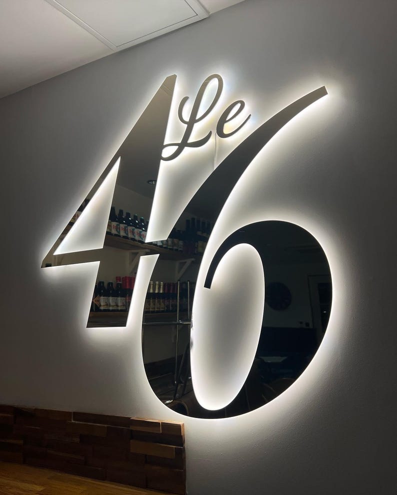 May include: A black and silver illuminated sign with the text "Le 46" in a cursive font.
