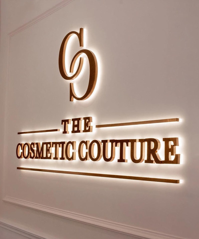 May include: A gold sign with the text "THE COSMETIC COUTURE" with a double "C" logo above the text.