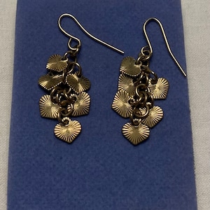 May include: A pair of gold dangle earrings with a cluster of heart-shaped charms. The charms have a textured, sunburst design.