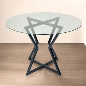 Op de afbeelding: Een ronde glazen tafelblad met een zwarte metalen onderstel. Het onderstel is gemaakt in de vorm van een geometrische ster.