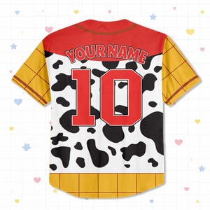 Op de afbeelding: Een honkbalshirt met korte mouwen met een rode juk en de tekst "YOUR NAME" boven een groot rood nummer "10". De trui heeft een witte body met zwarte koeienvlekken, gele mouwen en een gele zoom.