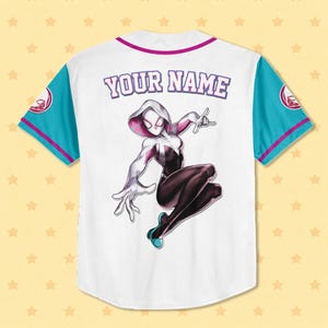 Puede incluir: Camiseta de b&eacute;isbol blanca con un gr&aacute;fico de Spider-Gwen. La camiseta tiene mangas turquesas con ribete rosa y un cuello rosa. El texto "YOUR NAME" est&aacute; encima del gr&aacute;fico. Una ilustraci&oacute;n de estilo c&oacute;mic de Spider-Gwen est&aacute; en la espalda.
