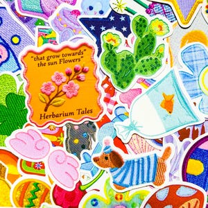 May include: A collection of colorful embroidered patches with various designs. Includes a patch with a cactus, a dog in a blue striped sweater, and a patch with the text "that grow towards the sun Flowers" and "Herbarium Tales".