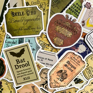 Op de afbeelding: Een verzameling vintage-stijl etiketten voor flesjes met toverdrankjes met fantasievolle illustraties en tekst. De etiketten tonen een verscheidenheid aan thema's, waaronder draken, vleermuizen en schedels. Sommige van de etiketten bevatten tekst zoals "Bat Drool", "Dragon Scales", "Skele-Gro" en "Amortentia".