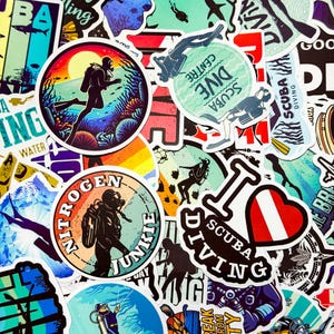 May include: A collection of colorful scuba diving themed stickers. Designs include divers, underwater scenes, and text such as "I love scuba diving" and "Nitrogen Junkie". The stickers feature various shapes and sizes, with a mix of illustrations and text.