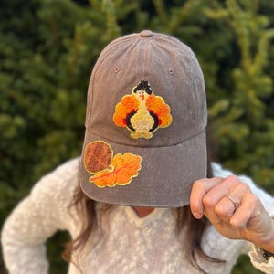 Distressed brown adjustable baseball hat with 2 chenille leaves on the bill and a chenille turkey patch on the front