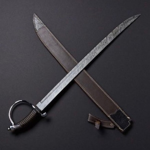 Peut inclure: Une épée argentée et noire avec une lame à motifs est posée sur un fourreau en cuir marron. L'épée a une poignée incurvée et une garde décorative. Le fourreau est cousu avec du fil blanc et a une extrémité texturée noire.