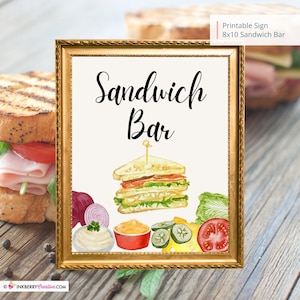 Może przedstawiać: Drukowana tabliczka 20x25 cm w złotej ramie z napisem "Sandwich Bar" czarnym, ozdobnym pismem. Pod tekstem znajduje się akwarelowa ilustracja kanapki typu club sandwich z sałatą, pomidorem, serem i ogórkiem.