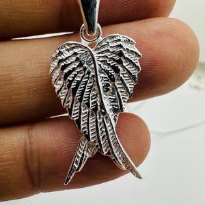 Puede incluir: Un collar con colgante plateado con un dise&ntilde;o detallado de ala. El colgante presenta intrincadas texturas en forma de plumas y cuelga de una delicada cadena. El colgante de ala mide aproximadamente 4 cm de largo.