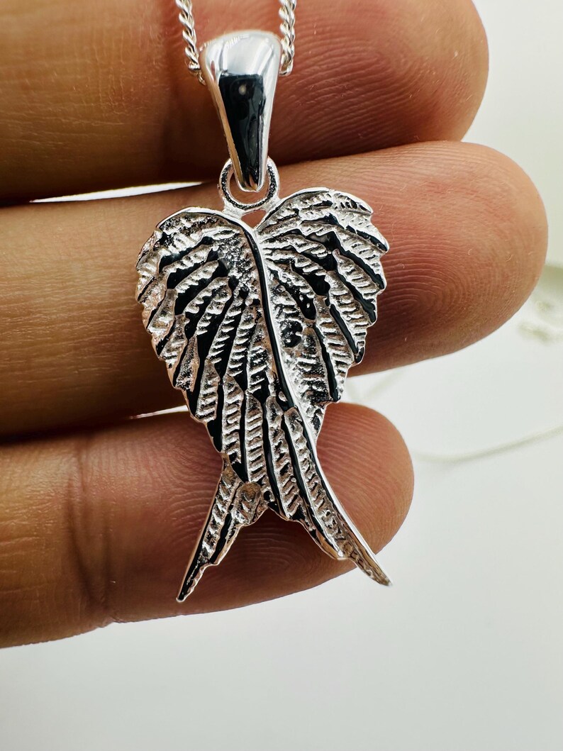 Puede incluir: Un collar con colgante plateado con un dise&ntilde;o detallado de ala. El colgante presenta intrincadas texturas en forma de plumas y cuelga de una delicada cadena. El colgante de ala mide aproximadamente 4 cm de largo.