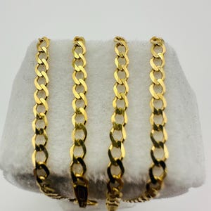 May include: Four gold-colored curb chains displayed on a white surface. The chains are linked together with a clasp. The links are oval-shaped and interlocked, creating a continuous pattern. The chains are likely made of metal.