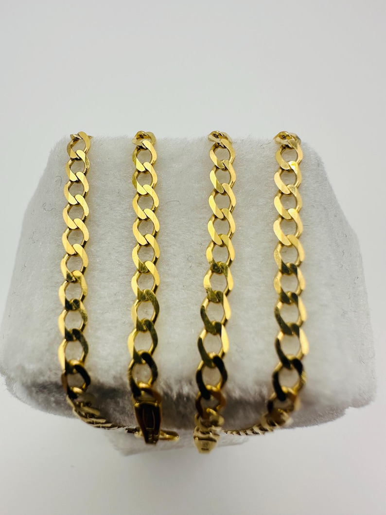 May include: Four gold-colored curb chains displayed on a white surface. The chains are linked together with a clasp. The links are oval-shaped and interlocked, creating a continuous pattern. The chains are likely made of metal.