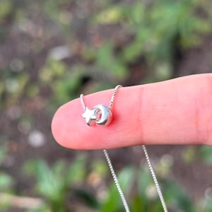 May include: A silver necklace with a small charm featuring a crescent moon and a star.