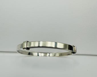 May include: A silver adjustable baby bracelet. The bracelet has a rectangular plate in the center and a clasp closure. The bracelet is made of shiny, polished metal and is set against a white background.