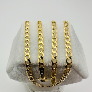 May include: A gold-colored curb chain necklace displayed on a white surface. The necklace is made of interlocking links and features a clasp. The chain is approximately 18 inches long.