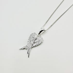 Puede incluir: Un collar plateado con un colgante en forma de alas de &aacute;ngel. Las alas, con texturas detalladas de plumas, cuelgan de una fina cadena. El colgante mide aproximadamente 2,5 cm de ancho.