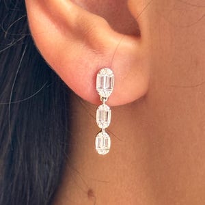 Może przedstawiać: Srebrne kolczyki wiszące z trzema owalnymi, przezroczystymi kamieniami szlachetnymi.