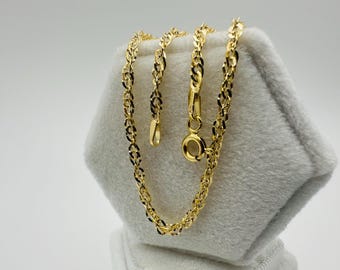 May include: A gold-colored chain necklace with a delicate, interwoven design. The necklace is displayed on a soft, white surface, showcasing its intricate links and clasp. The chain's warm hue contrasts with the neutral background.