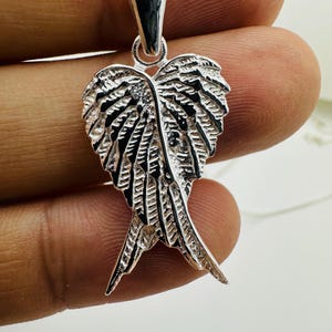 Puede incluir: Un collar con colgante plateado con un dise&ntilde;o de alas detalladas. El colgante tiene una superficie texturizada con intrincados detalles de plumas. La cadena del collar tambi&eacute;n es plateada y parece delicada.