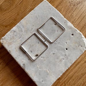 Op de afbeelding: Een paar zilveren vierkante creolen. De oorbellen zijn simpel en modern in design.