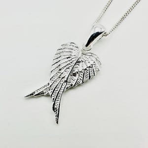 Puede incluir: Un collar con colgante plateado con un dise&ntilde;o de ala detallado. El colgante tiene forma de par de alas con intrincados detalles de plumas. El collar tiene una cadena delicada y un acabado pulido, adecuado para el uso diario.