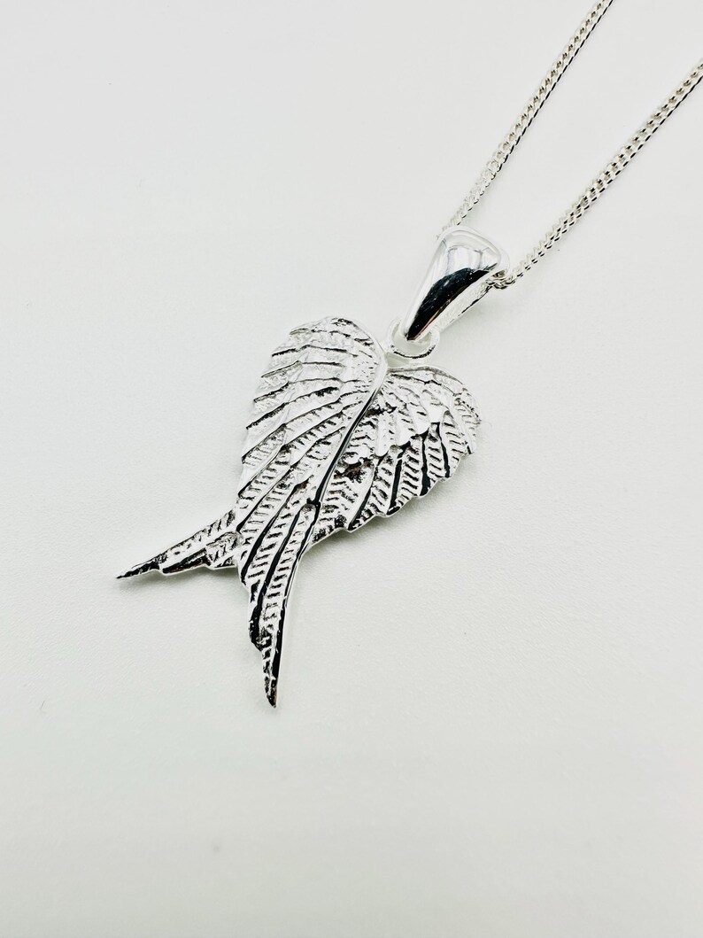 Puede incluir: Un collar con colgante plateado con un dise&ntilde;o de ala detallado. El colgante tiene forma de par de alas con intrincados detalles de plumas. El collar tiene una cadena delicada y un acabado pulido, adecuado para el uso diario.