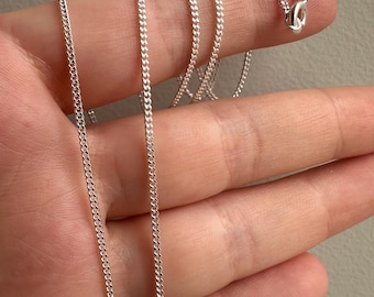 Könnte beinhalten: Eine silberne Curb-Kette mit einem Karabinerverschluss.