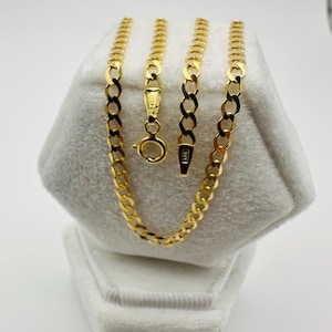 May include: A gold chain necklace with a curb link design, displayed on a white velvet jewelry box. The necklace is a bright, shiny gold color, with a lobster clasp closure. The chain is approximately 18 inches long.