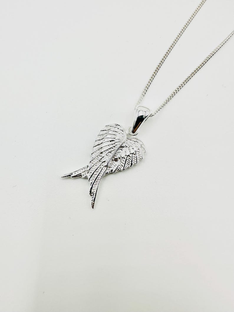 Puede incluir: Collar con colgante plateado con dise&ntilde;o de ala. El colgante, con detalles de plumas, cuelga de una fina cadena. Esta joya es sencilla pero elegante. Un accesorio cl&aacute;sico.