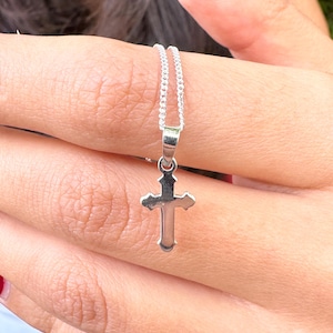May include: A silver chain necklace with a small, silver cross pendant.