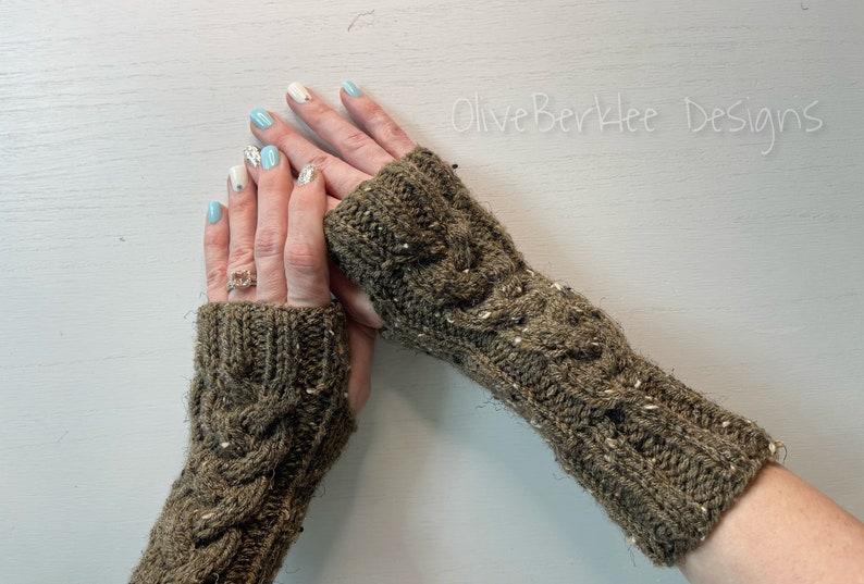 May include: A pair of brown knitted fingerless gloves with a cable knit pattern. The gloves are worn on a person's hands with light blue nail polish.