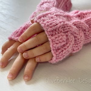 May include: Pink knitted fingerless gloves with a sparkly thread. The gloves are folded in half and the tips of the fingers are visible.