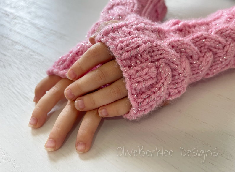 May include: Pink knitted fingerless gloves with a sparkly thread. The gloves are folded in half and the tips of the fingers are visible.