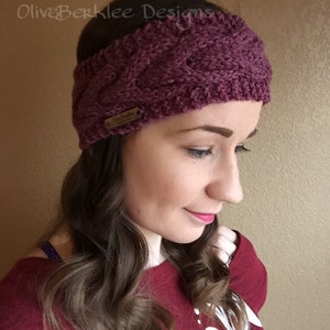 May include: A purple knitted headband with a cable knit pattern. The headband has a brown leather tag with the text "Olive Berklee Designs" on it.