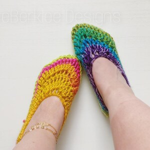May include: A pair of crocheted rainbow slippers. The slippers are made with a variety of colors, including pink, yellow, green, blue, and purple. The slippers are worn on a person's feet.