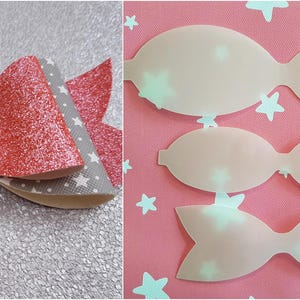 Op de afbeelding: Een handgemaakte haarstrik met een glitterende koraalafwerking en een stervormige versiering. De strik heeft lagen grijze stof met witte sterpatronen. De afbeelding toont ook strijksjablonen met steruitsparingen op een roze achtergrond.