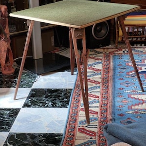May include: A unique, mid-century modern table with a square, green felt top. The table has slender, angled wooden legs and a speaker built into the frame. The table is approximately 30 inches tall.