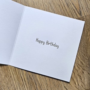 Peut inclure: Une carte blanche avec le texte "Happy Birthday" &eacute;crit en encre noire.