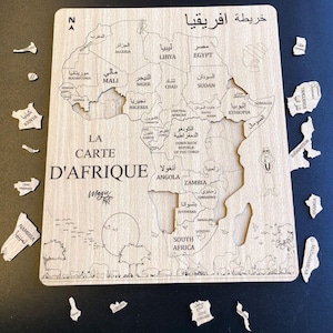 May include: A wooden jigsaw puzzle of the African continent with each country outlined and labeled in Arabic and English. The puzzle pieces are scattered around the board. The title of the puzzle is "La Carte D'Afrique Magic Art".