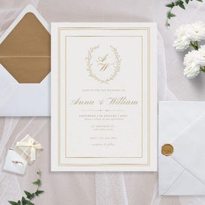 May include: Elegant wedding invitation with gold accents. The invitation features a floral wreath with the initials "A & W". The text reads "Join us for the wedding of Anna & William". Includes matching envelopes and a ring box.