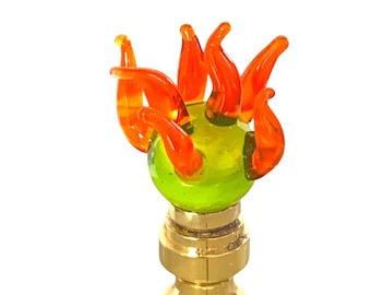 May include: A decorative lamp finial featuring a green glass orb with orange flame-like accents. The finial is mounted on a brass base, creating a striking contrast of colors and textures. This unique piece adds a touch of artistic flair to any lamp.