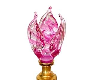 May include: A pink glass flower finial with a gold metal base. The flower is made of clear glass with pink swirls and a pink center.