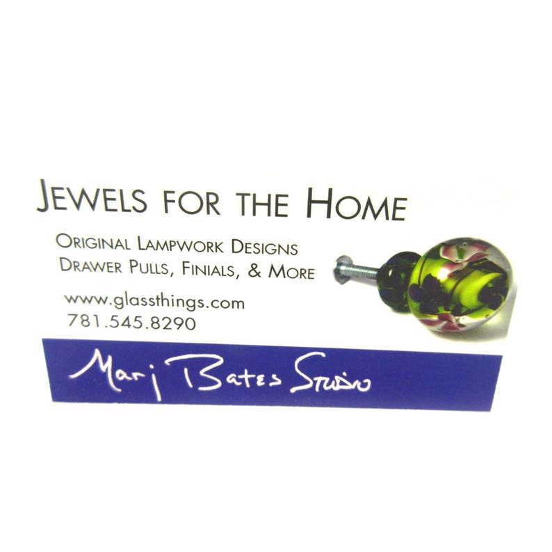 May include: A business card with the text "JEWELS FOR THE HOME" and "ORIGINAL LAMPWORK DESIGNS". A decorative glass drawer pull with green, pink, and black accents is on the right. The website is www.glassthings.com.